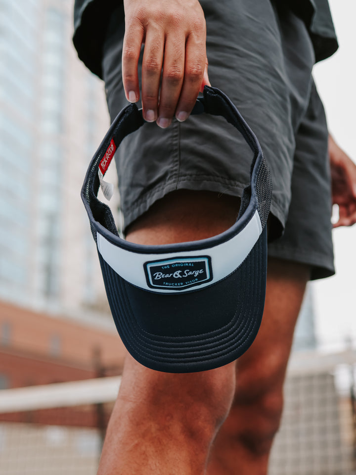 Hand holding navy Retro B+S trucker visor on pickleball court — Bear & Sarge